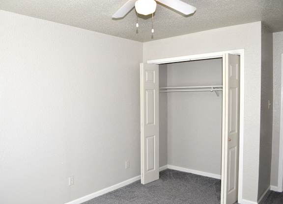 A white closet with a ceiling fan and a door.