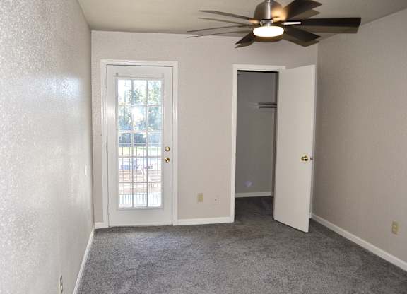 A room with a ceiling fan and a door leading to a balcony.