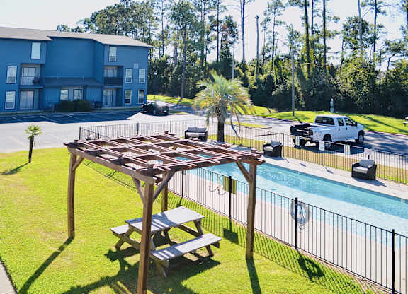 A wooden pergola is over a picnic table by a pool.
