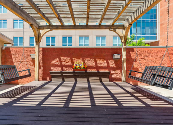 a patio with benches and a swing in front of a building