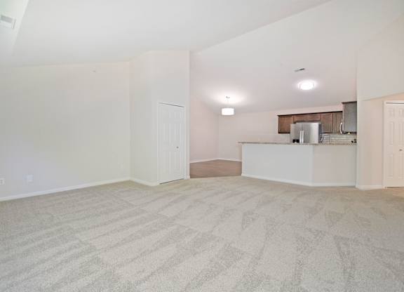 A room with a carpeted floor and a kitchenette in the corner.