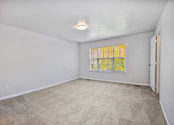 A room with a carpeted floor and a window with bars.