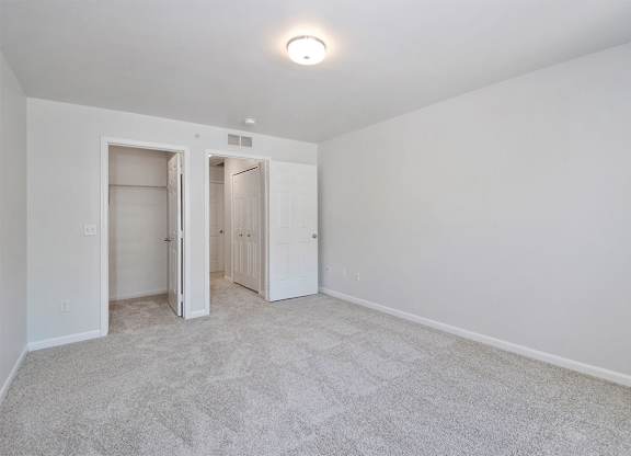 A white bedroom with a carpeted floor and two open doors.