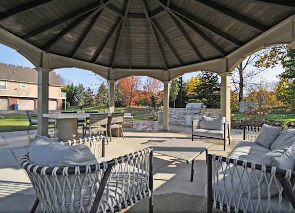 A gazebo with grey couches and a table is surrounded by trees.