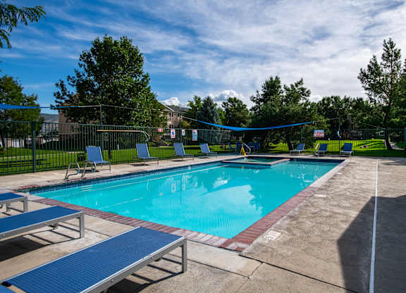 A blue pool with a diving board and lounge chairs.