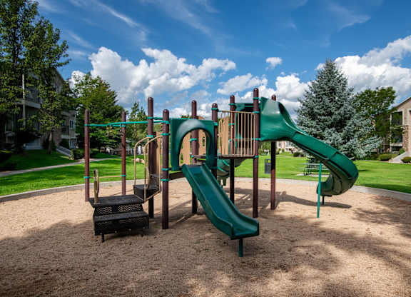 A playground with a green slide and a brown sandbox.