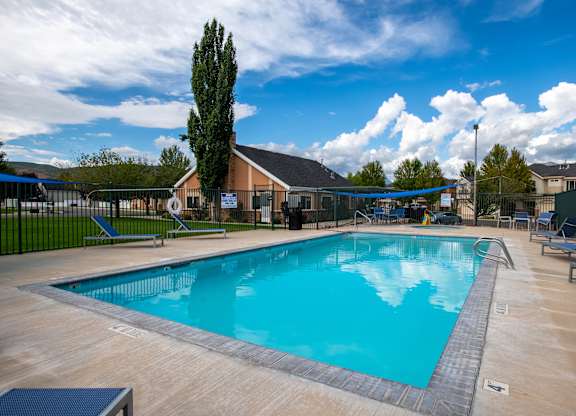 A large outdoor swimming pool surrounded by a fence and lounge chairs.