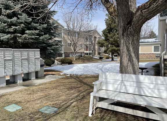 A white bench sits in the foreground of a snowy landscape with a building in the background.