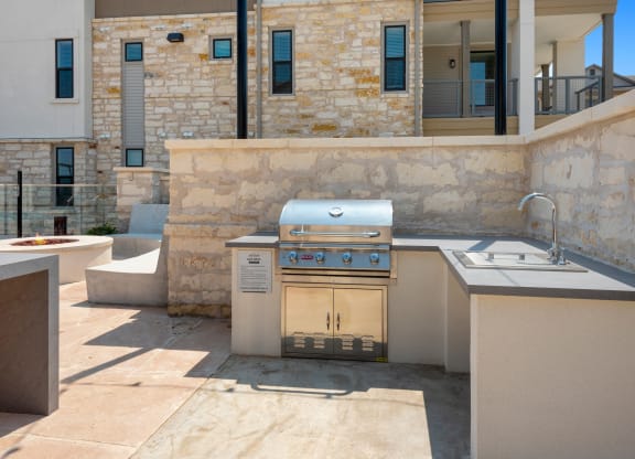 an outdoor kitchen with a grill and a sink in a backyard