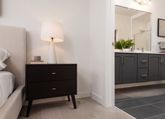 a bedroom with a black nightstand with a lamp and a bathroom with a sink