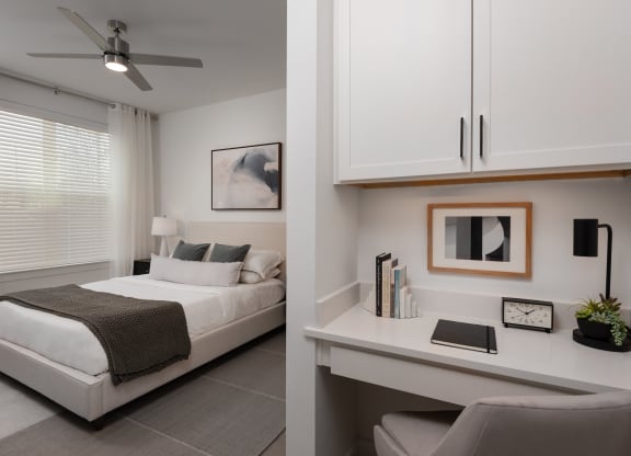 a bedroom with a white bed and a desk and a window