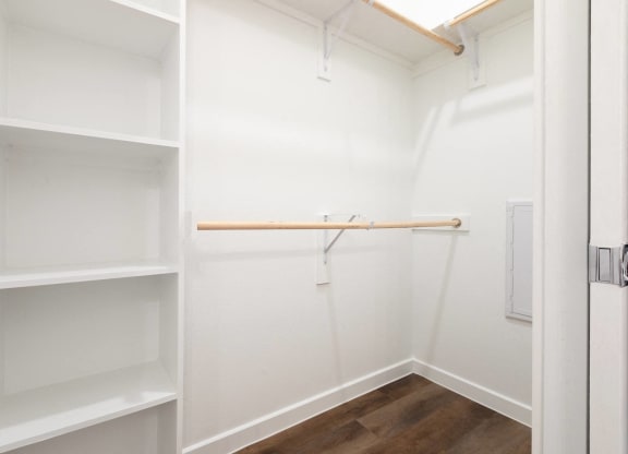 a walk in closet with white shelves and a wood floor