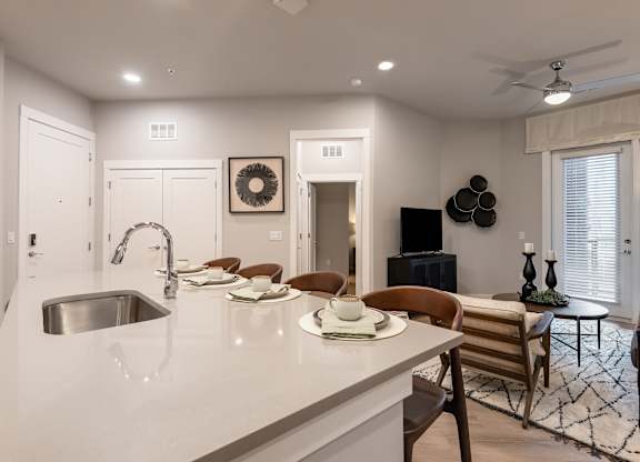 A modern kitchen with a white countertop and a dining area with a round table and chairs.