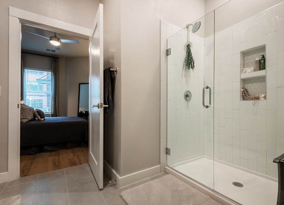 A bathroom with a walk-in shower and a bedroom with a window.