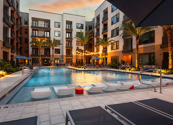 A pool surrounded by palm trees and lounge chairs.