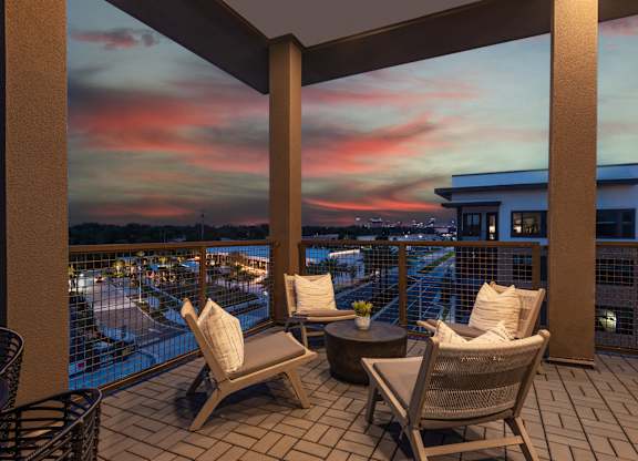 A balcony with chairs and a table overlooking a body of water at dusk.