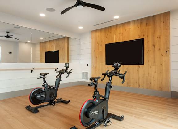 Two exercise bikes are placed in a room with wooden walls.
