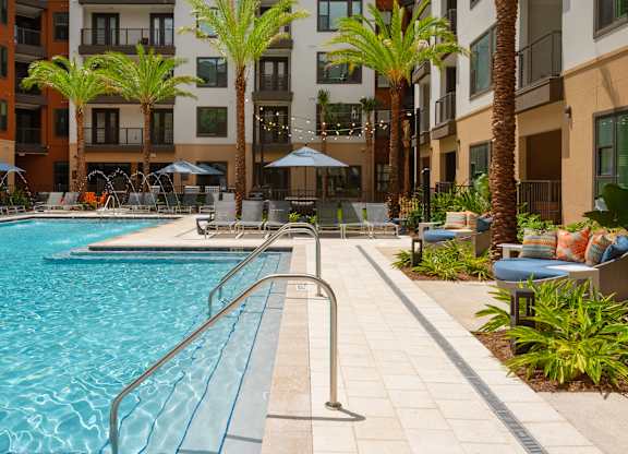 A pool surrounded by palm trees and a building in the background.
