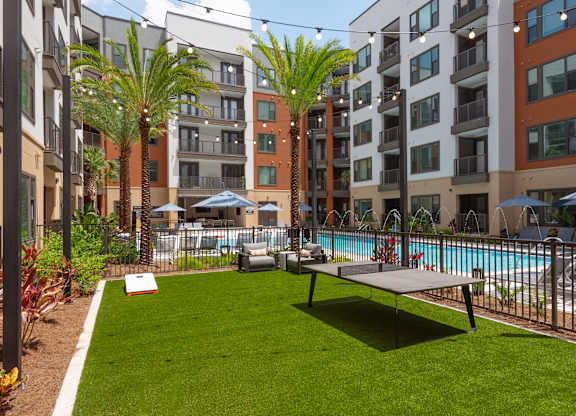 A grassy area with a pool and apartment buildings in the background.