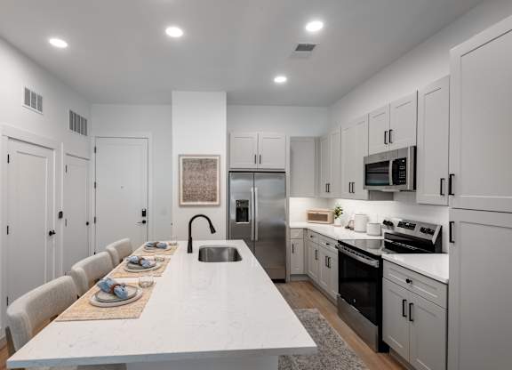 A modern kitchen with a long white table and chairs.