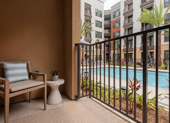 A chair with a blue pillow is on a patio next to a pool.