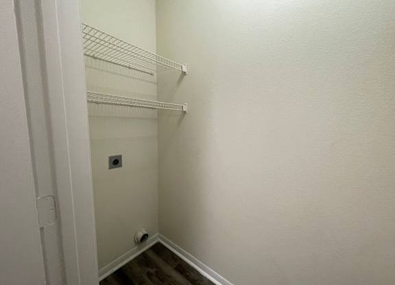 A white closet with a door open and a light switch on the wall.