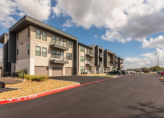 A street view of a residential area with apartment buildings on the left and cars parked on the right.