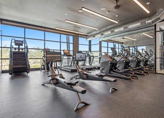 A gym with a row of treadmills and exercise bikes.