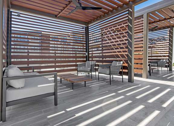 A patio with a couch, chairs, and a table with a ceiling fan.