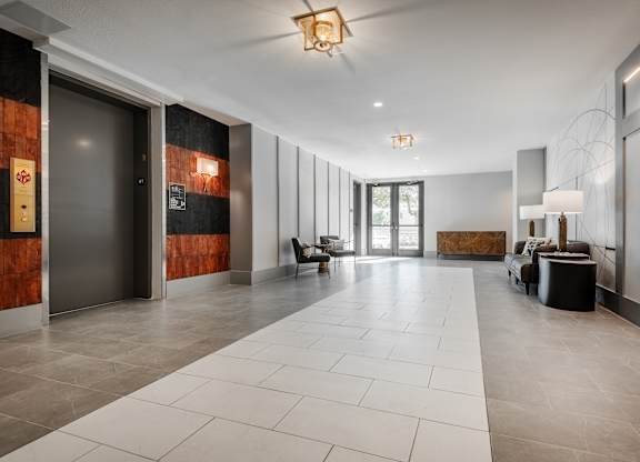 the lobby of a condo with a large white tiled floor and a glass door
