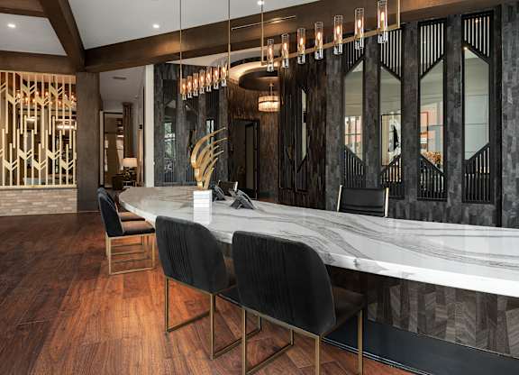 a long marble bar with black chairs and a staircase in the background