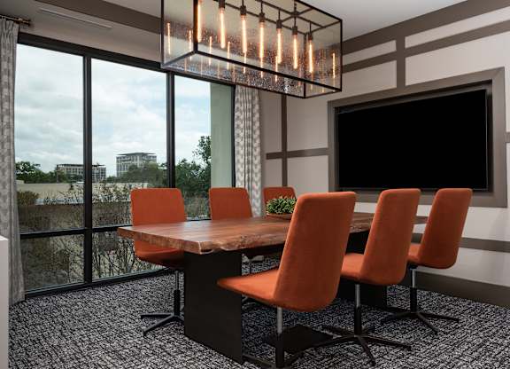 a conference room with a large screen tv and a wooden table with orange chairs