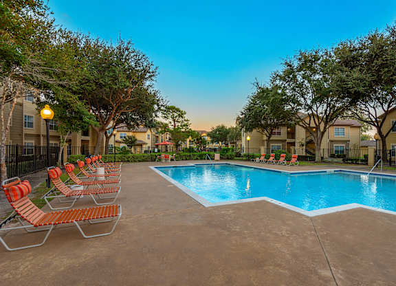 A swimming pool surrounded by orange chairs and trees.