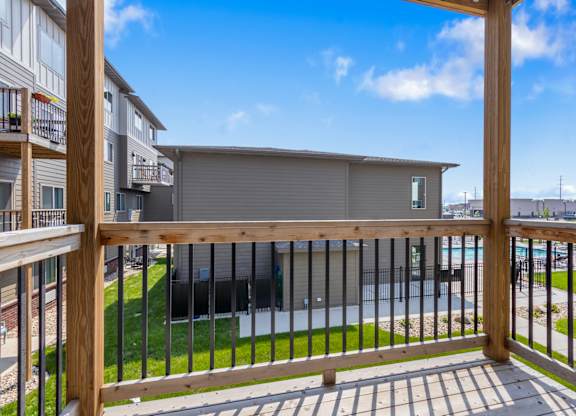 A balcony with a wooden railing overlooks a grassy area and a building.