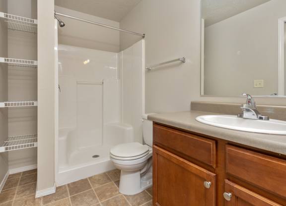 A white toilet sits in a bathroom next to a sink and a walk-in shower.
