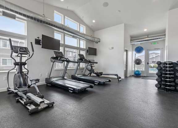 A spacious gym with treadmills, elliptical machines, and a weight rack.