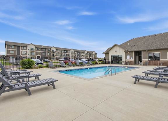 A swimming pool surrounded by lounge chairs in front of apartment buildings.