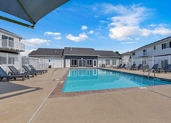 A swimming pool surrounded by sun loungers and apartment buildings.