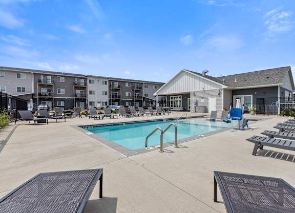 A large swimming pool surrounded by a concrete patio and lounge chairs.