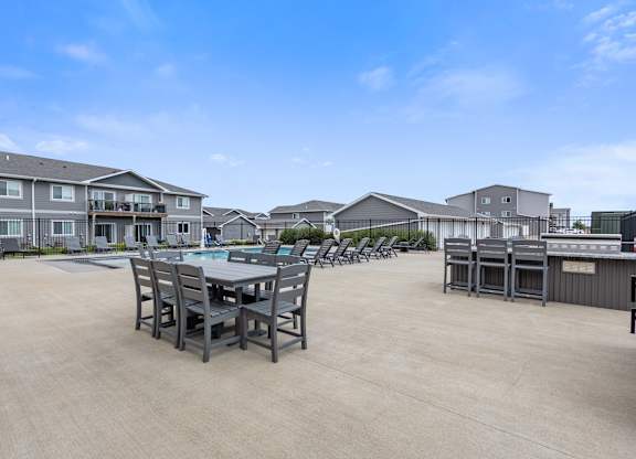 A large outdoor dining area with a table and chairs is surrounded by residential buildings.