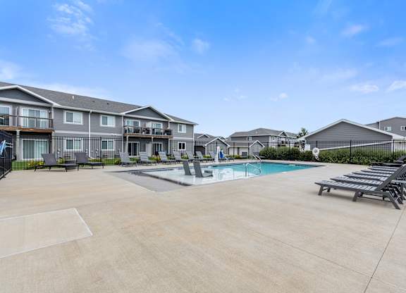 A sunny day at a residential complex with a pool and loungers.