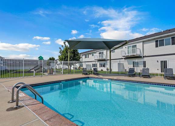 A swimming pool in front of a building with a white fence and trees.