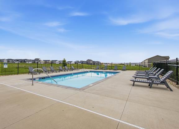A pool surrounded by a black fence with sun loungers on the side.