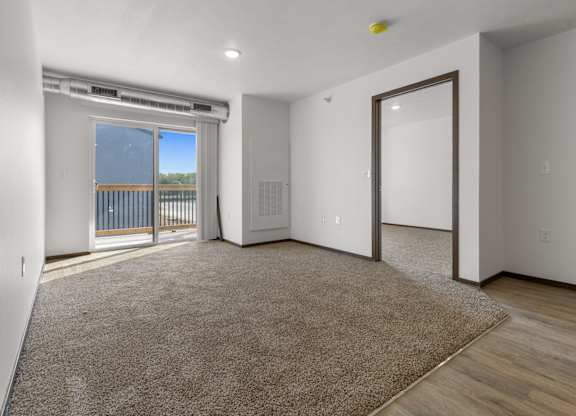 A spacious room with a carpeted floor and a sliding glass door leading to a balcony.
