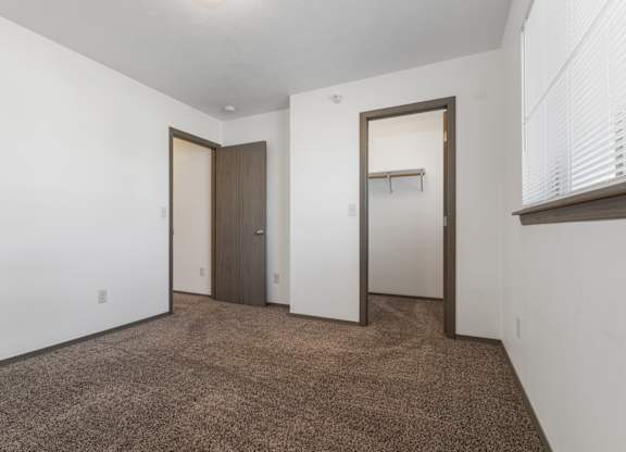 A room with brown carpet and white walls with two doors.