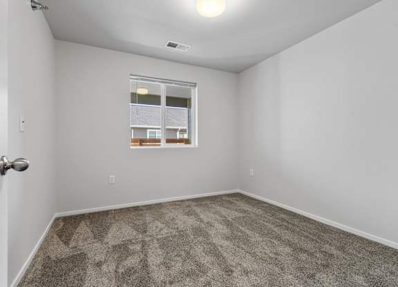 A room with a carpeted floor and a window showing a view of a building.