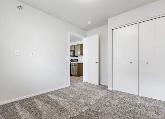 A room with white walls and a carpeted floor with a white door on the right.