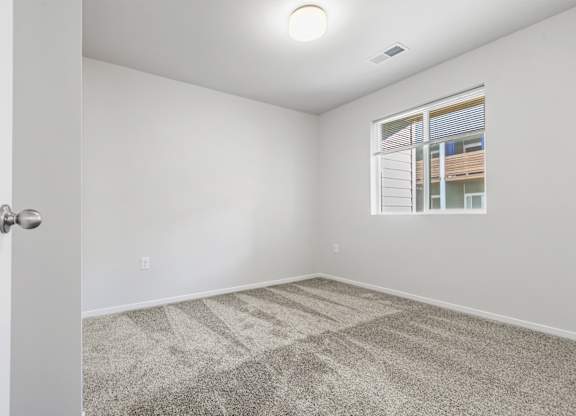 A room with a carpeted floor and a window showing a building outside.