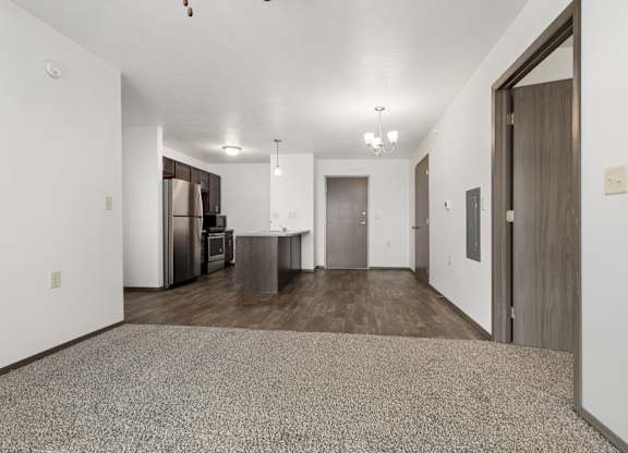 A spacious room with a carpeted floor and a kitchen area in the background.