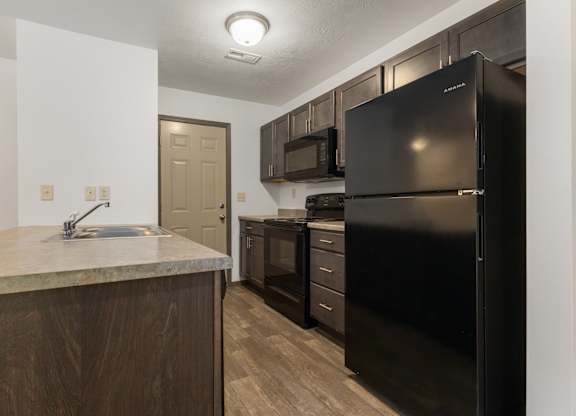A kitchen with a black refrigerator and wooden cabinets.